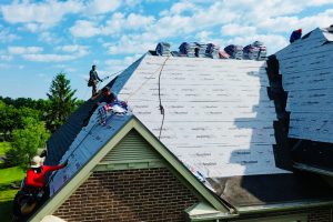 Fan 1 - Integrity 1st Roofing Workers on a sloped house roof installing roof underlayment, with tools and safety harnesses visible beside bags of materials under a blue sky