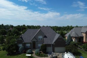 Fan 3 - Integrity 1st Roofing Suburban two-story brick house with a gray shingle roof; ladder leaning to the front, with construction materials and a van in the driveway.
