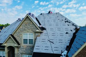 Fan9 - Integrity 1st Roofing Two-story house undergoing roof renovation with blue roofing underlayment covering most of the roof surface.