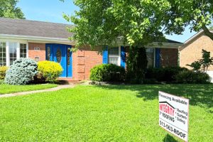 item_07f9b1cd-8e63-444a-bd0e-ab046a3ef17a - Integrity 1st Roofing Brick ranch-style house with blue front doors and a well-kept lawn; a lawn sign advertises Integrity Roofing with financing and the phone 513-563-ROOF.