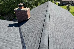 item_233fcc70-a740-4525-ab8a-937b35af56b1 - Integrity 1st Roofing Aerial view of a house roof with gray asphalt shingles, a brick chimney on the left, and a vent running along the ridge.