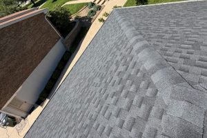 item_2d3feda5-6ffc-41d9-b014-4ebbeaeaa509 - Integrity 1st Roofing Aerial view of a gray shingle roof with a brick building and green landscaping on the left, and a concrete path along the sidewalk below.