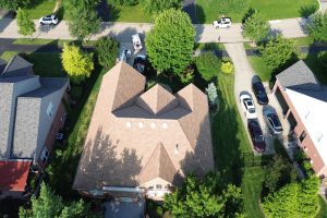 item_9fb8085e-e833-41ee-935b-4777a6d430c5 - Integrity 1st Roofing Aerial view of a suburban neighborhood with a large brown-roofed house surrounded by green lawns and tree-lined streets.