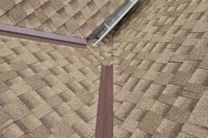 item_b4eeba14-ae4f-4b2d-8372-4212c0ea7d44 - Integrity 1st Roofing Close-up of brown shingle roof where two planes meet at a valley, with brown metal flashing and a white vent/downspout along the edge.