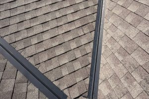 item_d3b52a25-b170-44e0-b6ac-430b36b06f3e - Integrity 1st Roofing Close-up of intersecting asphalt shingle roof sections with metal flashing forming a V-shaped seam.