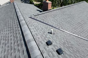 item_e66c53ec-0f07-400f-83d2-e056f098e5a8 - Integrity 1st Roofing Aerial view of a gray shingled roof with a white vent pipe, two black square roof vents, and a metal ridge cap.