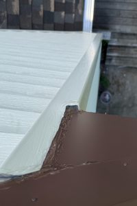 2c448b17-3041-411b-8d72-1c2f1c0be20b-item_ef39bb13-d0a0-4b68-b211-f7ab4fb32f8f - Integrity 1st Roofing Close-up of a roof edge: white flashing over a brown metal roof with sealant along the seam.