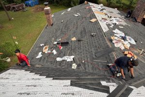 3c2e84a0-76fe-445d-9c99-b8b1f53af328-item_82c589fc-7a71-44c3-b7d5-ab95cd1835bf - Integrity 1st Roofing Two workers install dark roof shingles on a sloped roof, with underlayment and tools scattered around on the surface.