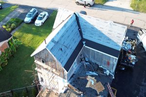 426e6ce3-a4af-4b08-baeb-ef83c6d22786-item_0e81d27e-4037-42f7-acde-f364b837a468 - Integrity 1st Roofing Aerial view of a two-story house under construction with scaffolding, a partially shingled roof, and a nearby debris-filled truck bed on the street outside.