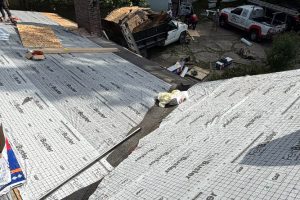 759cf6aa-868d-4898-9cd3-0800fe621672-item_fc28a016-799c-449a-9918-64d683d15ba1 - Integrity 1st Roofing Pitched roof under construction with silver underlayment panels; construction vehicles visible in the background.