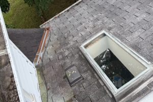 Roof Replacement16 - Integrity 1st Roofing Bird's-eye view of a shingled roof with an open rectangular skylight showing dark water inside.