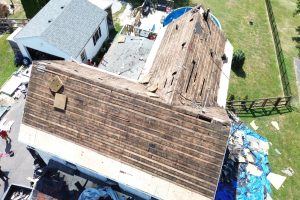 d1b6a247-feac-44b8-abc0-1bf19873c355-item_b72d9c8a-f4ac-411d-9ed1-cbf0b2f686af - Integrity 1st Roofing Aerial view of a house undergoing roof replacement, with a brown, partially stripped roof and construction debris nearby.